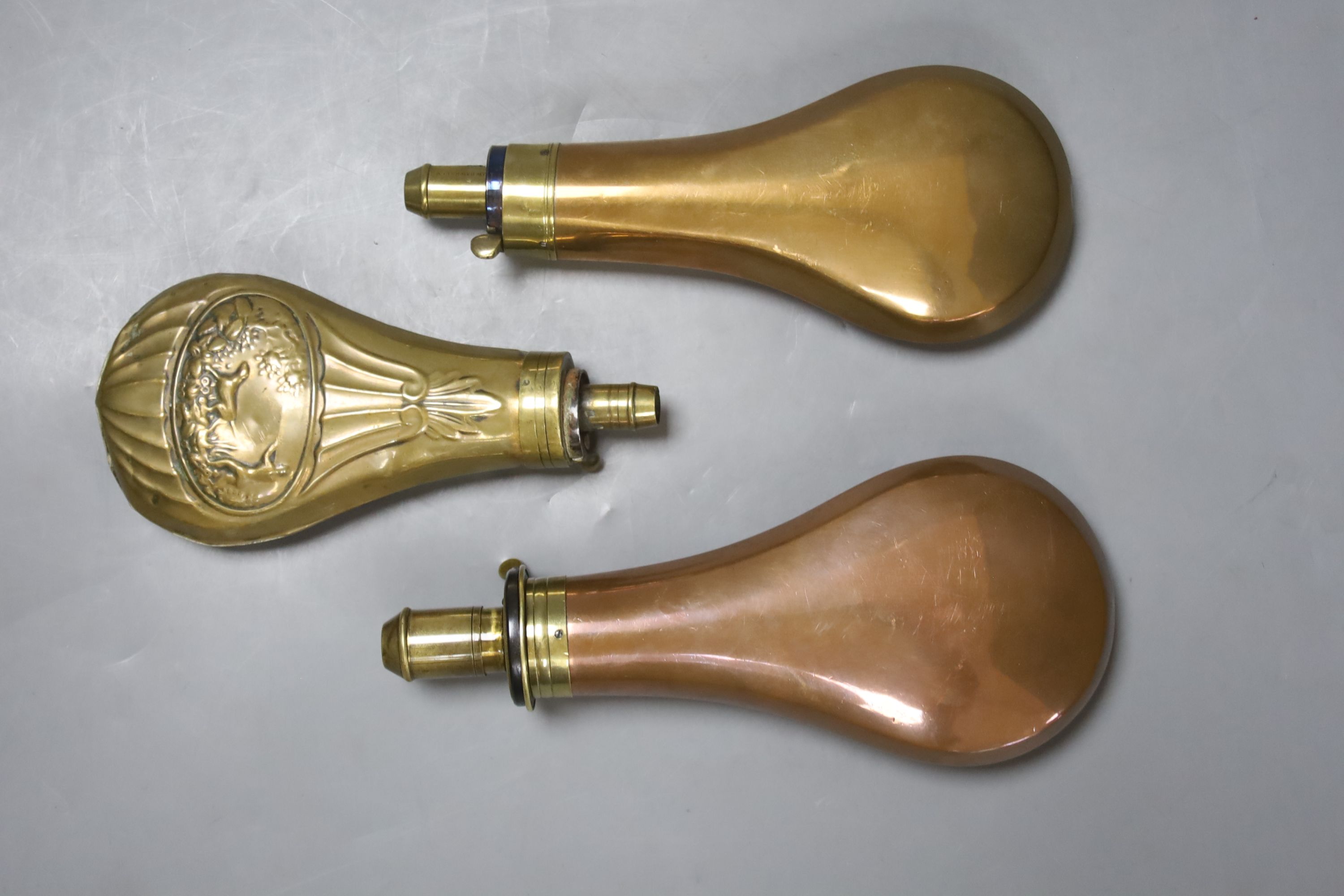 An 19th century embossed brass powder flask and two copper powder flasks, one with 4 drams capacity